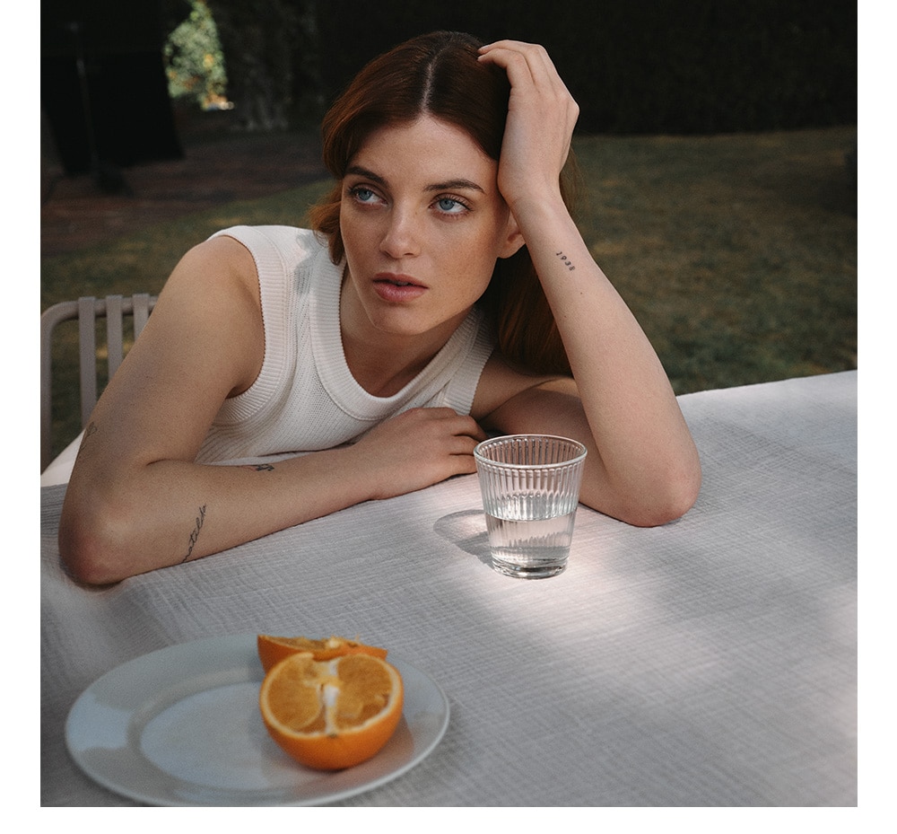 Nostalgic looking women sitting by the table with glass of water and half orange on a plate