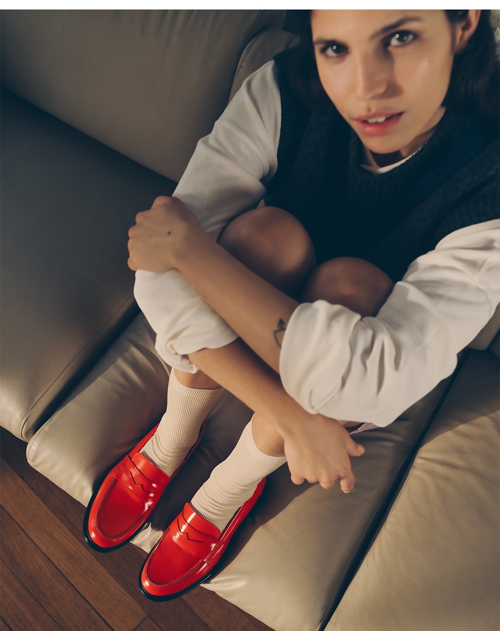 female model wearing red loafers sitting on a sofa