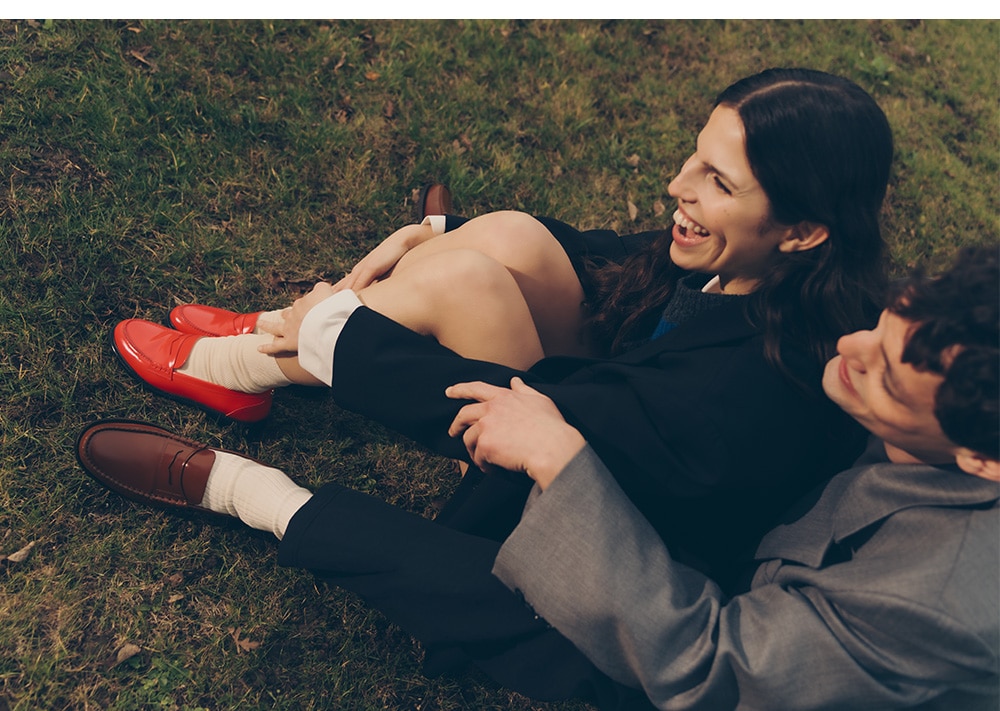 happy model couple sitting on the grass wearing red and brown loafers