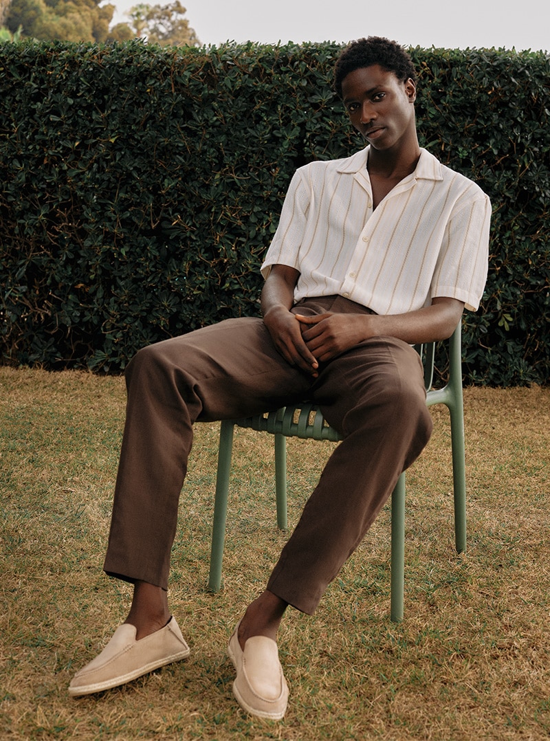 Man sitting on chair wearing taupe suede slip-on Russell and Bromley shoes; Di Marme