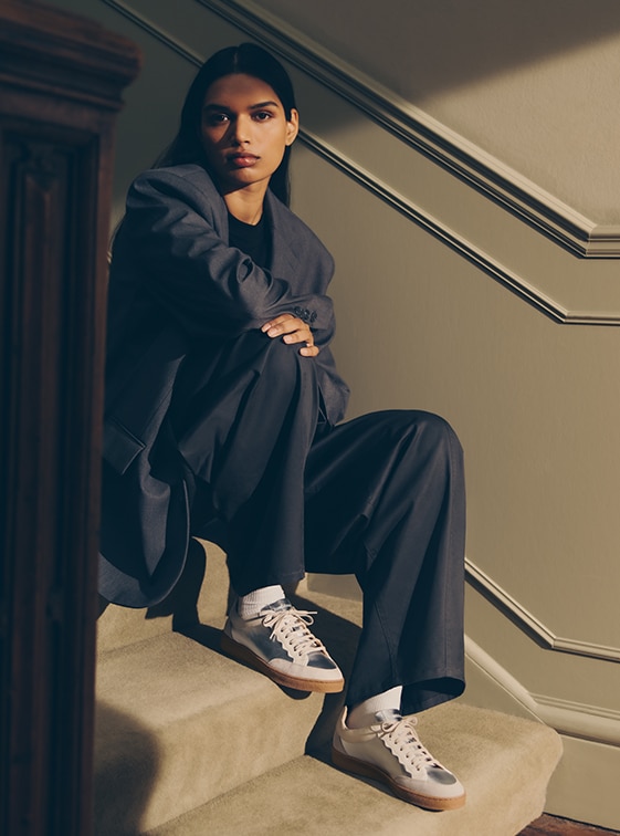 Woman sitting on stairs, wearing navy blue suit and Russell and Bromley silver trainers; Roller