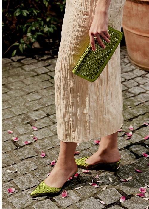 Female model wearing Russell and Bromley Kitty heeled loafer and holding Kitty clutch bag