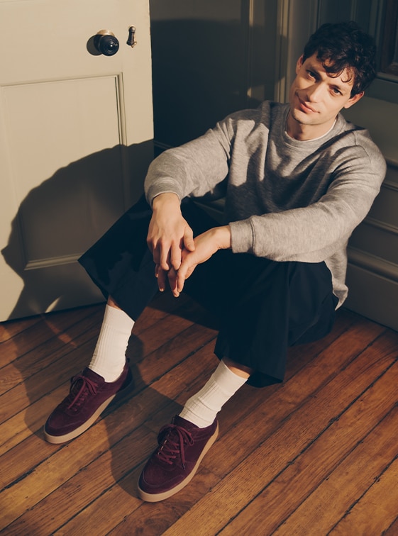 Man sitting on the floor, wearing Russell and Bromley burgundy suede lace-up trainers; Rebound