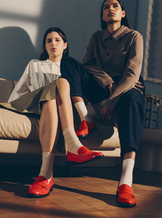 Women sitting on sofa wearing red leather patent Russell and Bromley loafers; Penelope